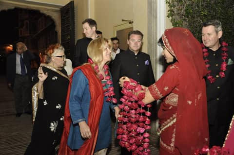 Guests being welcomed with marigold garlands by woman in red sari