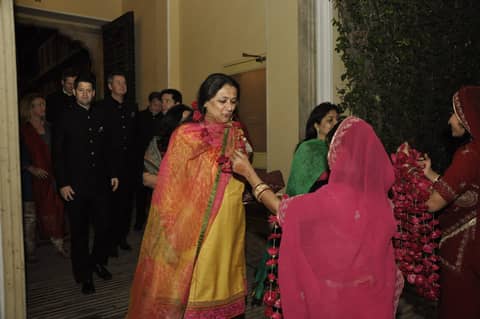 Woman in pink/orange sari being welcomed with garlands
