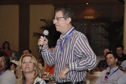 Man with microphone speaking at session; Gayle seated in front
