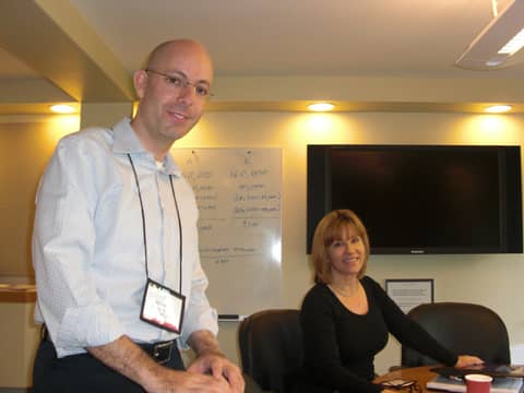 Man in shirt and lanyard standing; woman seated behind